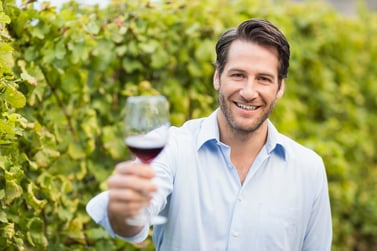 Young happy man smiling at camera and holding a glass of wine in the grape fields