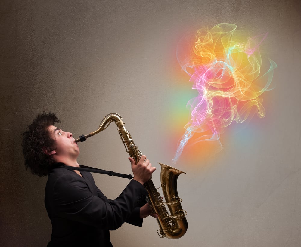 Attractive young musician playing on saxophone with colorful abstract fume coming out